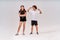 Two teenagers having workout. Happy boy showing his biceps to a cute smiling girl, standing isolated over grey