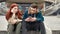 Two teenagers spending time together, sitting on the steps outdoors. Upset girl looking at her boyfriend while he is