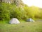 Two tents stand in a forest with mountains in background.