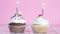 Two testy sweet cup cakes with cream and burning candles on the table