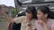 Two Thai lovely teen sisters enjoy taking selfie photo together with mobile smartphone while sitting at rear side of hatchback car