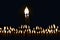 Two thin candles stretch their lights towards each other. Their fire merges into one flame. The candles are in complete darkness.