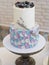 Two-tier cream cake in blue-gray-lilac colors, decorated with blueberries and sprigs of lavender on black stand. Wedding