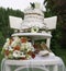 Two-tiered cake, spring bouquet and white bride`s shoes on a white wooden chair - outside