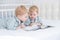 Two toddler baby twin boys in pajamas reading book lying in his parents bed