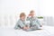 Two toddler baby twin boys in pajamas reading book sitting on white bedding on bed