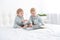 Two toddler baby twin boys in pajamas reading book sitting on white bedding on bed