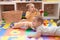 Two toddlers sucking maraca sitting on floor at kindergarten