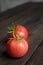 Two tomatoes on a wooden table. The first harvest of tomatoes. On the table are two red tomatoes with tails. green