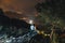 Two tourists on top of the mountain. Climbing, hiking trail. View of the night city. Romantic setting. Couple in love back view,