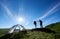 Two tourists with trekking sticks in backpacks give each other high five near camping in mountains