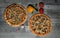 Two traditional pizzas on a gray wooden rough background, next to the decoration of spicy herbs, tomato, olives, Bulgarian pepper