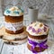 Two traditionally baked orthodox paskas with glace icing and bright blue and violet flowers on white woooden background