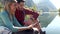 Two travel hikers using mobile phone while sitting in front of the lake in mountain.