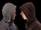 Two troubled teenage boys with black hoodie standing in front of each other in profile isolated on black background - stock