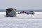 Two trucks sit parked on the ice near an ice fishing shanty.