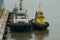 Two tugboats with blue hull and white and yellow superstructure moored.