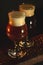 Two tulip beer glasses on dark wooden table over black background. Dark and light beer, stout beer, wheat beer.