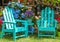 Two turquoise Adirondack chairs and a matching table surrounded by beautiful flowers and trees and shining mirror balls handing fr