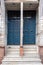 Two twin blue wooden doors with stone staircase and dividing post. Vertical photo