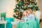 Two twin sisters sitting in a turquoise chair in the hall for the New Year. A sister whispers a secret in her ear in a decorat