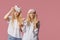 Two twin sleepless young women in pajamas and sleep masks on a pink background.