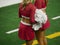 Two unrecognizable cheerleaders stand in the sideline of a football field