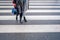 Two unrecognizable persons in black shoes cross wet street after rain on crosswalk, red umbrella, parallel lines