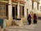 Two unrecognizable women in traditional Tibetan clothes walk down dusty road.