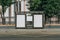 Two vertical blank white billboards at bus stop on city street. In the background buildings and trees. Mock up.