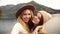 Two very happy attractive girls young women fashionably dressed on vacation on a lake in the mountains shoot video chat