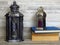 Two very old silver lanterns and a pile of old books on bleached oak background.