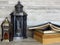 Two very old silver lanterns and a pile of old books on bleached oak background.