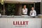 Two waiters standing in front of a Lillet summer bar with its logo and glasses.
