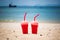 Two watermelon smoothies in disposable plastic cups with tubes. On a sandy tropical beach. Against the backdrop of the blue sea.