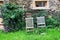 Two weathered woden chairs standing in the garden outside a rustic old stone barn