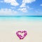 Two wedding rings in a heart lei on beach vacation. Hawaiian flower necklace lying on the sand in the shape of a heart with rings