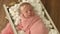 Two-week-old baby girl with a rim on her head wrapped in a pink blanket peacefully sleep in a wooden cradle