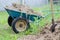 Two-wheeled wheelbarrow with earth located near shovel on the grass