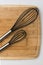 Two Whisks Angled on a Wooden Cutting Board