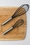 Two Whisks Angled on Wooden Cutting Board on White Background