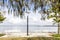 Two white benches sit on the waters edge. It is morning and the ocean is calm. Tree branches overhang the top of the image