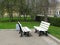 Two white benches stand opposite each other in the park. Benches