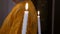 Two white burning candle in the hands of bride and groom at glans in Orthodox chirch background of a priest