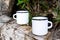 Two white campfire enamel mug mockup with tree stump