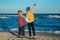 Two white Caucasian children kids, older sister and younger brother playing paper planes on ocean sea beach on sunset