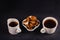 Two white ceramic cups of healing infusion of birch mushroom chaga with chaga pieces in bowl on black with copy space