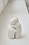 Two white ceramic figurines for salt and pepper in a human form are hugged on a white surface.