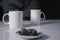 Two white cups of tea next to used tea bags on white table in gray kitchen