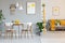 Two white lamps above a round dining table in open space apartment interior with yellow blanket on gray sofa. Real photo